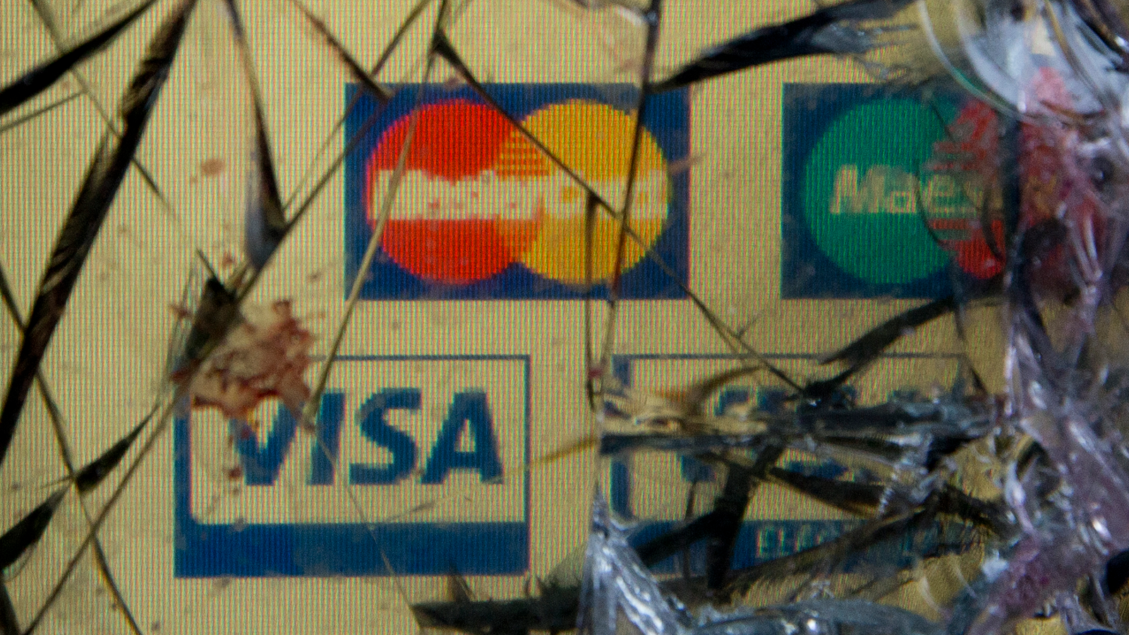 A vandalized ATM machine displaying the logos of major credit cards on a cracked screen.