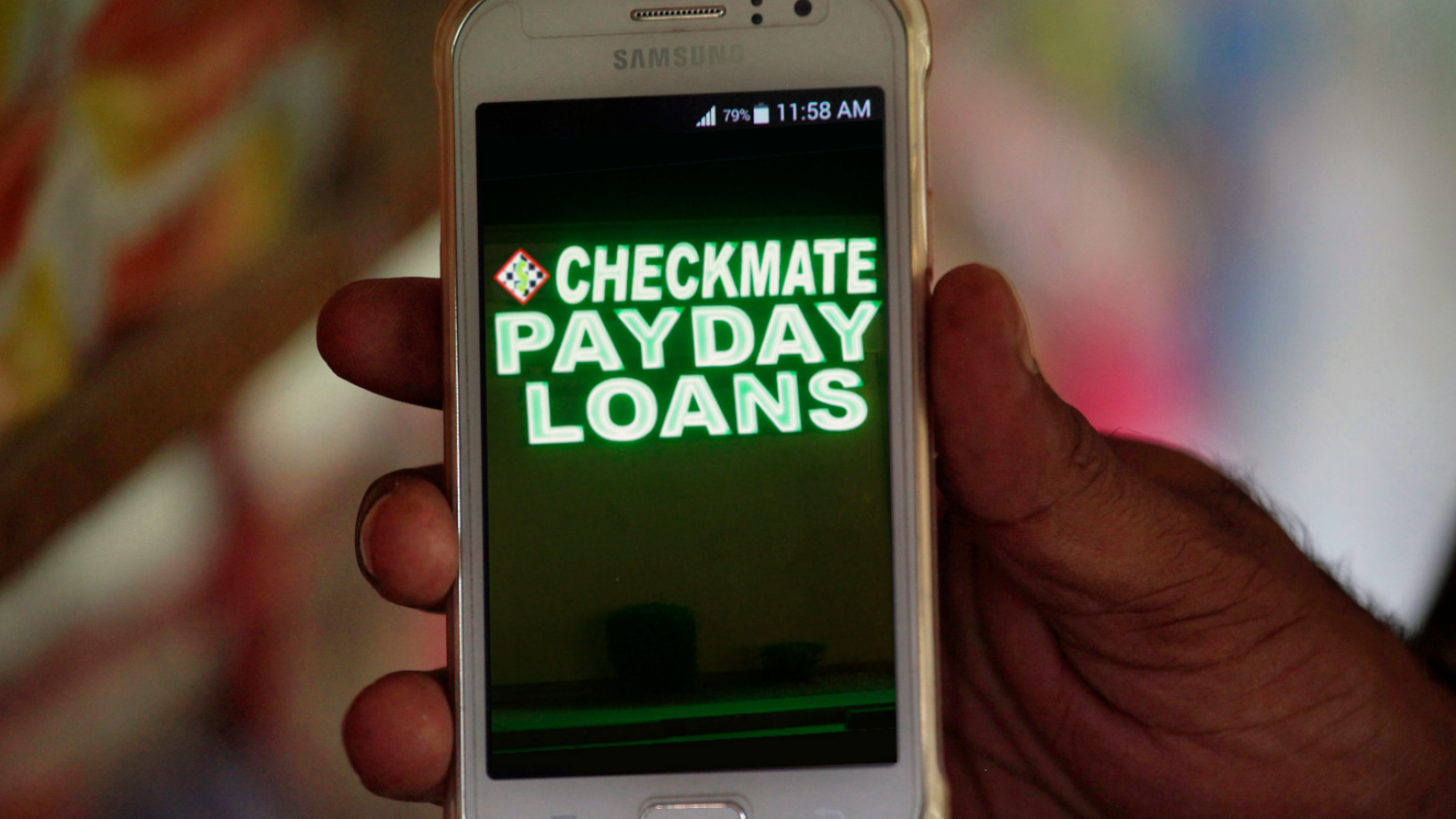 A composite image showing a hand holding a smartphone with a neon payday loan business sign superimposed on the screen.