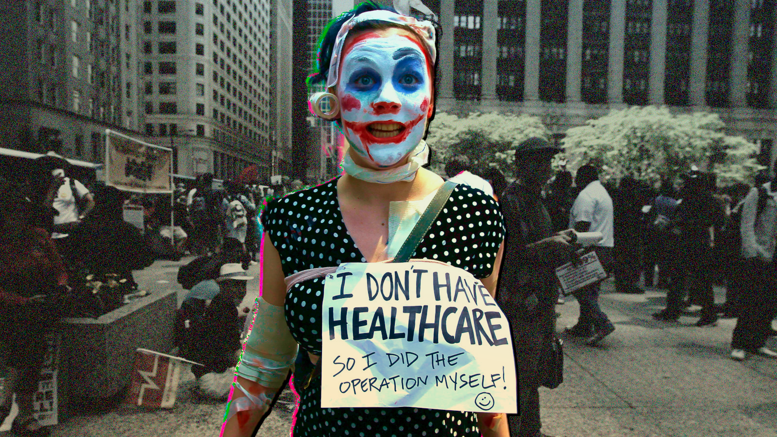 A protester at a healthcare demonstration wears a sign stating, “I don’t have healthcare, so I did the operations myself!”