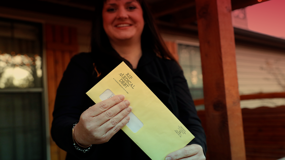 Reagen Adair holds on to an RIP Medical Debt yellow envelope on the front porch of her home. (AP Photo/Tony Gutierrez)