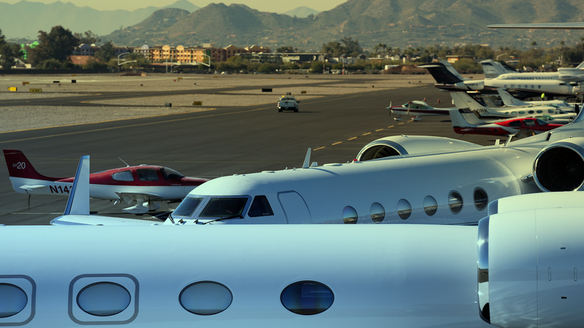 Private planes sit parked on the tarmac as the Scottsdale Airport in Arizona with mountains in the distance.